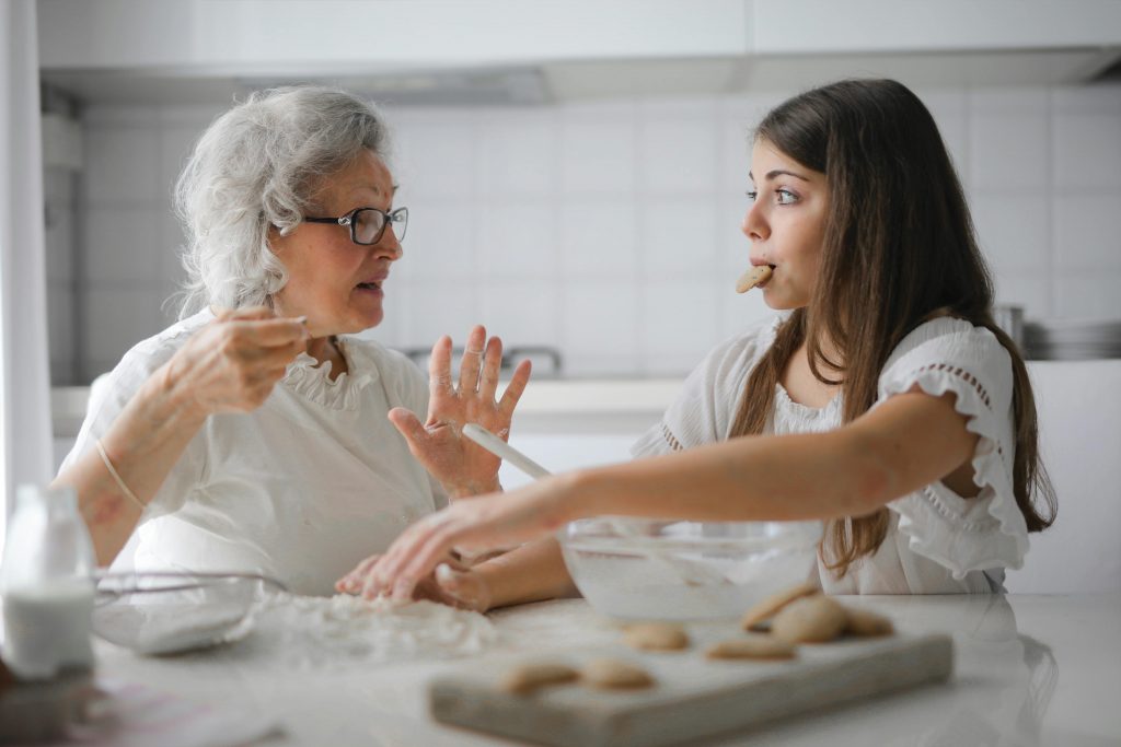 Nastolatka i starsza kobieta w okularach jedzą ciastka i rozmawiają o chorobach wieku starczego.