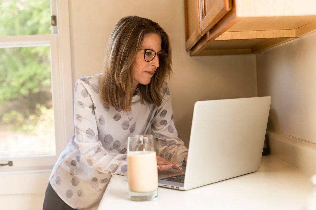 Kobieta w okularach stoi w kuchni i czyta artukuł na temat krwawienia po menopauzie.